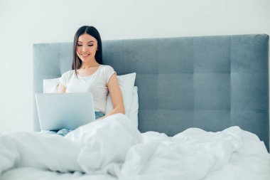 Evde dinlenen ve dizüstü bilgisayar ekranına bakıp gülümseyen olumlu bir genç kadın. Web sitesi afişi
