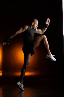 Yakışıklı kaslı adam, turuncu ışık arka planında koşarken ayağını ve dizini kaldırıyor.