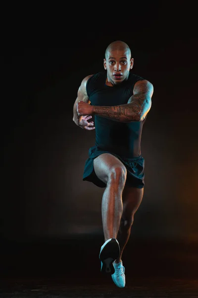 Muscular bold sportsman expressing determination while running against the dark background