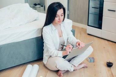 Sakin bir bayan odasında yerde oturuyor ve modern bir dizüstü bilgisayarın ekranına yapışkan bir not yazıyor.