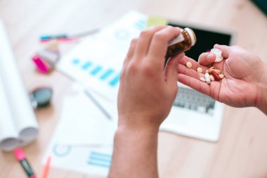 Tanınmayan bir adamın elinde küçük bir cam şişeyle ilaç alırken çekilmiş bir fotoğrafı. Web sitesi afişi