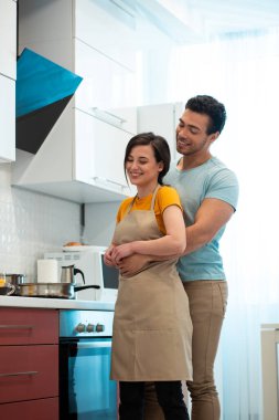 Neşeli, güler yüzlü bir kız arkadaşın arkasında durup onu kucaklayan olumlu bir adam.