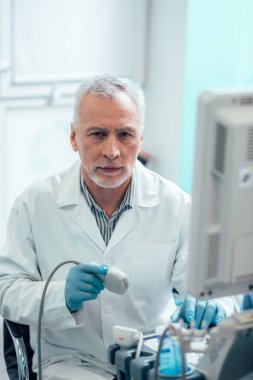Klinikte modern ultrason dönüştürücü kullanırken lastik eldiven takan kendinden emin bir doktor.