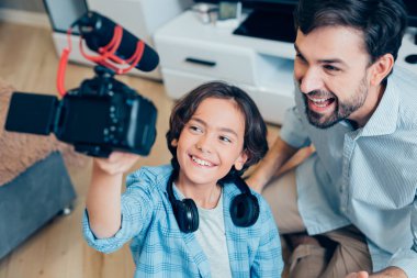 Neşeli çocuk mikrofonlu bir kamera tutuyor ve kendisinin ve pozitif babasının videosunu kaydediyor.