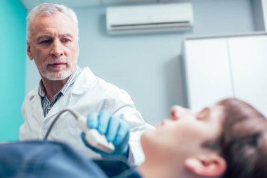 Olgun Kafkas doktoru, ultrason dönüştürücü ve tiroit bezini tararken hastanın boynuna bakıyor.