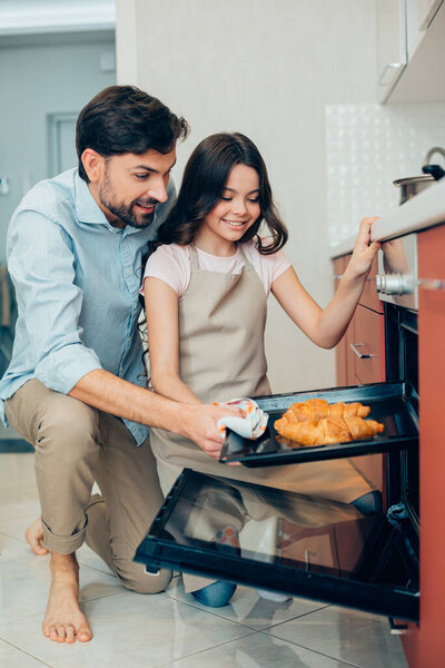 Позитивная красивая девушка и ее отец берут сковородку со свежими круассанами из духовки