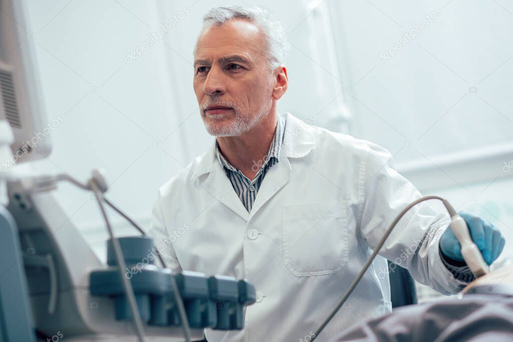 Confident concentrated medical worker looking at the screen during the procedure of abdominal sonogram