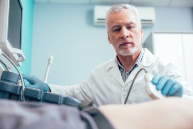 Lastik eldivenli profesyonel sonograf hastanın karın organlarını incelerken dönüştürücü kullanıyor.