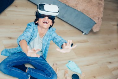 Mutlu çocuk yüzündeki sanal gerçeklik aygıtı karşısında heyecanlı görünüyor ve ellerini ileri uzatırken gülümsüyor. Web sitesi afişi