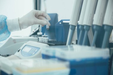 Modern bir laboratuvar ekipmanının kesilmiş fotoğrafı ve mikro test tüpü tutan bir laboratuvar uzmanının eli.