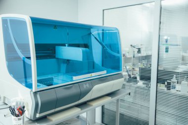 Modern bir kliniğin profesyonel laboratuvarına yerleştirilmiş mavi cam kalkanlı immünokimya analizcisi.