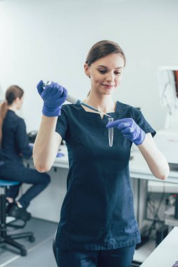 Gülümseyen hevesli laboratuar bilim adamı elinde boş bir test tüpü tutuyor ve içine pipet kutusuyla madde bırakıyor.