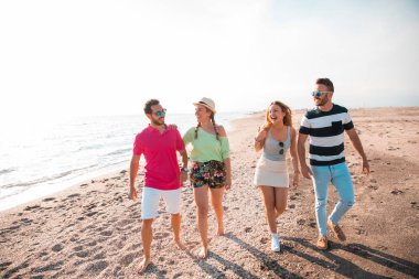 Güzel yaz günbatımında sahilde yürüyen bir grup mutlu genç. Arkadaşlar ve tatil konsepti