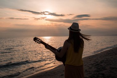 Gitar çalmak ve plaj güzel bir gün batımı sırasında dans genç bir kadın silueti. Müzisyen ve şarkıcı kavramı.