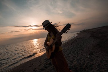 Gitar çalmak ve plaj güzel bir gün batımı sırasında dans genç bir kadın silueti. Müzisyen ve şarkıcı kavramı.