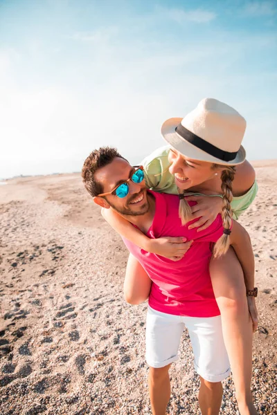 Handsome and happy man carrying his smiling girlfriend on back in paradisiac beach. Holiday and Couple in love concept