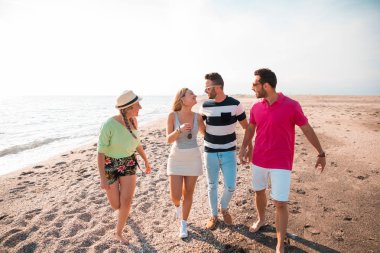Güzel yaz günbatımında sahilde yürüyen bir grup mutlu genç. Arkadaşlar ve tatil konsepti