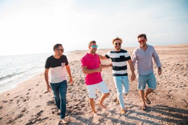 Güzel yaz günbatımında sahilde yürüyen bir grup mutlu genç. Arkadaşlar ve tatil konsepti