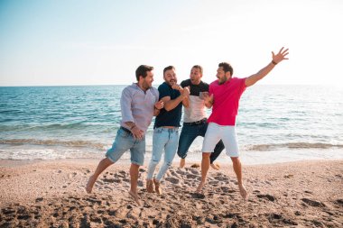 Group of happy young people jumping at the beach on beautiful summer sunset. Four best men friends. Friends and holiday concept  clipart