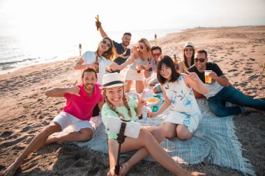 Multicultural group of friends partying on the beach  happy young people celebrating during summer vacation. summer time and holidays concepts. clipart
