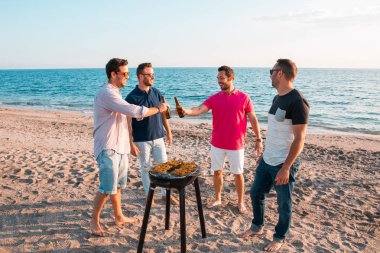 Happy friends are having fun while they are preparing a barbecue on the beach. Vacation concept. clipart