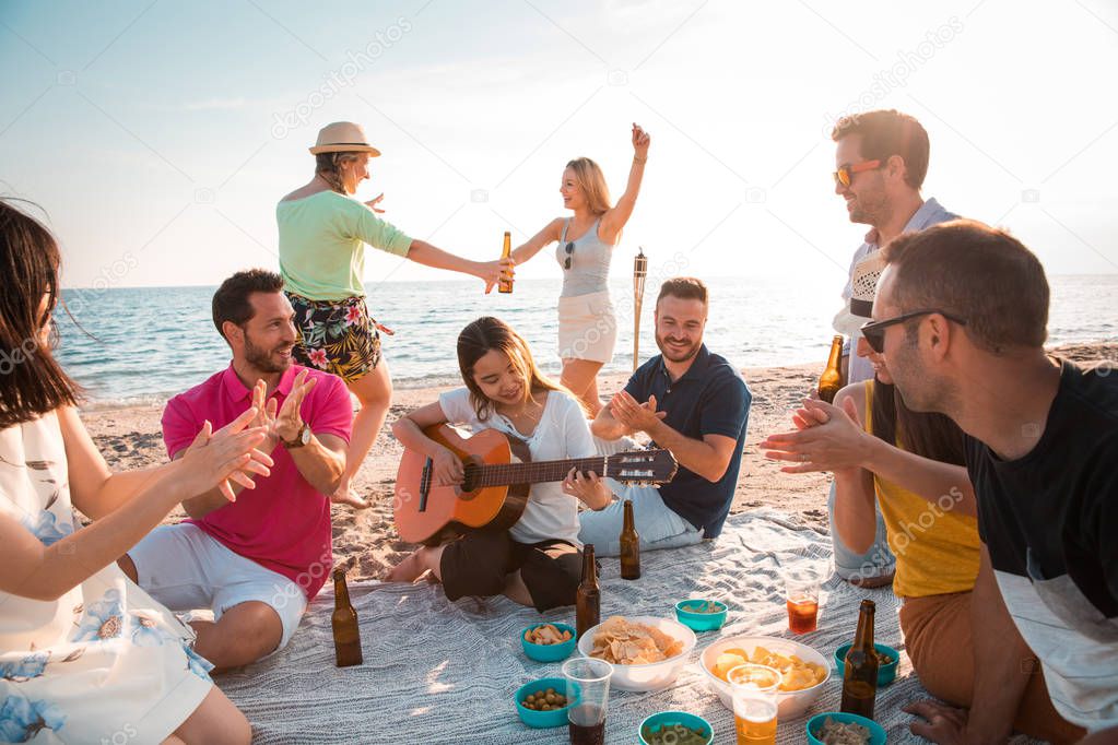 Multicultural group of friends partying on the beach  happy young people celebrating during summer vacation. summer time and holidays concepts.