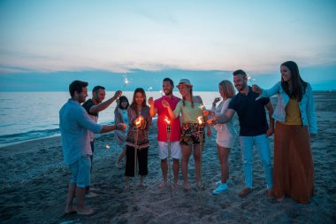 Group of happy friends lighting their sparkler during a party on the beach. Summer time. clipart