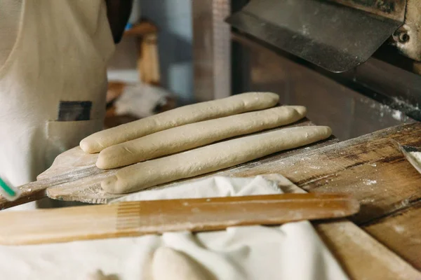 Baker ahşap bir fırında pişirme önce çiğ hamur ekmek hazırlanıyor. Geleneksel ekmek kavramı.