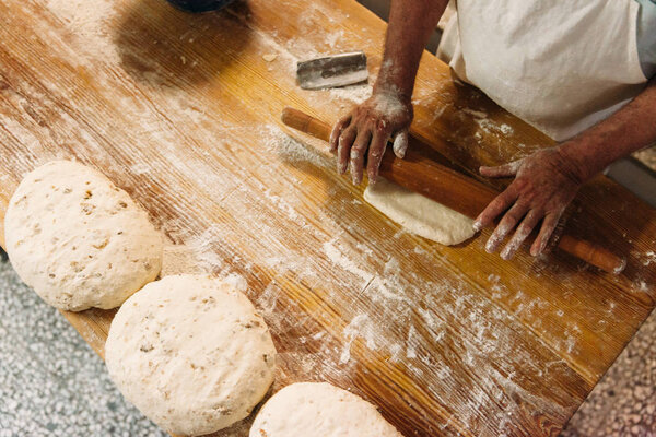 Male baker prepares bread. Baker kneading the dough with flour. Making bread. Top view. Rustic and traditional style.