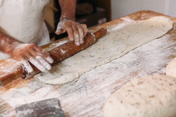 Male baker prepares bread. Baker kneading the dough with flour. Making bread. Rustic and traditional style of Bakery.