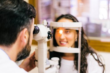 göz doktoruna muayene odasında göz testi makine bakarak sandalyesinde oturan genç kadınla