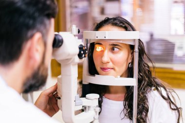 göz doktoruna muayene odasında göz testi makine bakarak sandalyesinde oturan genç kadınla