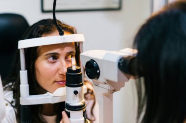 göz doktoruna muayene odasında göz testi makine bakarak sandalyesinde oturan genç kadınla