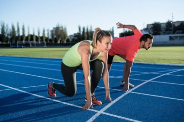 Athlete couple at starting position ready to start a race. Sprinters ready for race on race track. Woman against man. clipart
