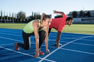 Athlete couple at starting position ready to start a race. Sprinters ready for race on race track. Woman against man. clipart