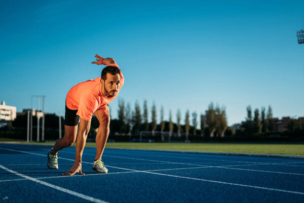 Young athlete man at starting position ready to start a race. Sprinters ready for race on race track.