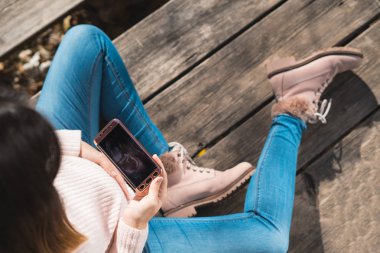 En iyi görünüm güzel hamile görünümlü ultrason resmin içinde onun hareket eden telefon. Hamilelik, sağlık, kadın hastalıkları, tıp kavramı. Genç bebek bekleyen anne. 