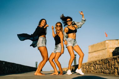 Gülümseyen ve giyen kot günbatımında atlama üç genç kadın portresi.