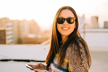 New York'ta bir terasta onun smartphone kullanarak güneş gözlüklü genç gülümseyen kadın