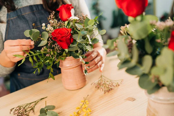 Woman florist makes a red roses bouquet on wooden table