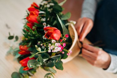 Çiçekçi kadın, ahşap masada turuncu lale buketi yapıyor.