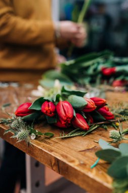 Adam çiçekçi kırmızı lale çiçek buketi ahşap masaya sağlar.