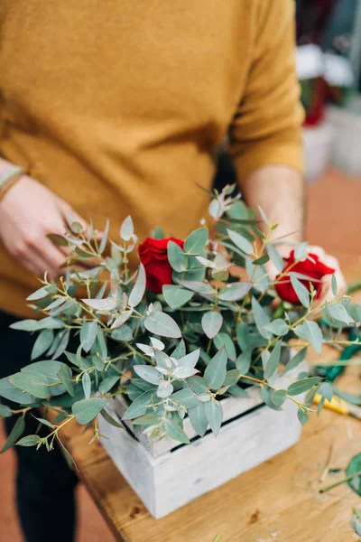 Man florist makes flowers bouquet in wooden box on a table