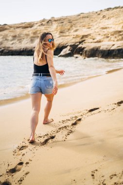 Yaz tatili boyunca sahilde yürüyen güzel genç bir kadın.