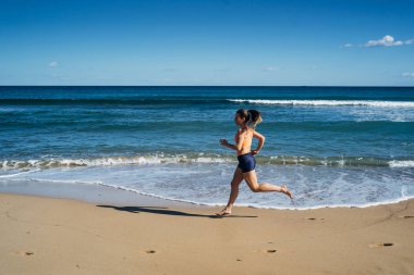 Yaz tatili boyunca plajda koşan genç bir kadın.