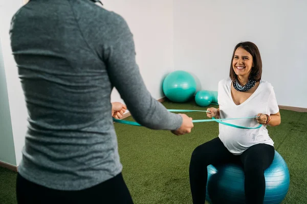 Pregnant woman doing fitness ball and pilates exercise with coac