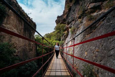 Deri çantalı bir kadının asılı bir köprüden ormana geçişi..