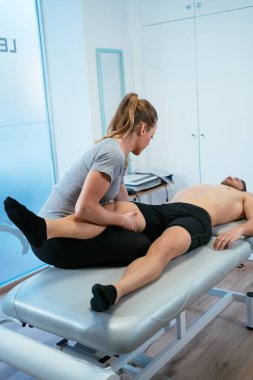 Yataktaki kadın fizyoterapistin dikey görüntüsü. Erkek bir müşteriye kuadriseps ve bacak masajı yapıyor. Kas sağlığı ve rahatlama kavramı.