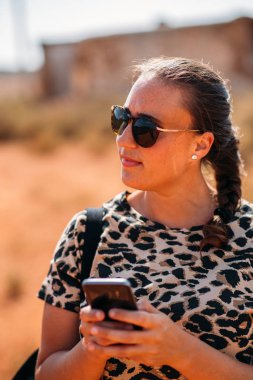 Dışarıda akıllı telefonunu kullanan genç ve güzel bir bayana yaklaş. Güneş gözlüğü, saç örgüsü ve hayvan desenli tişörtle gülümseyen neşeli kadın..