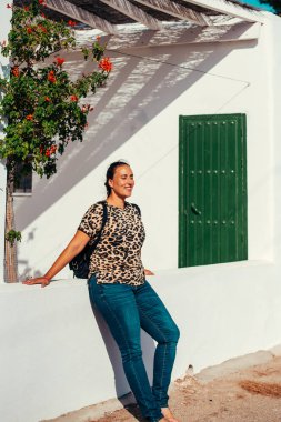 Terasta yeşil bir kapının yanında oturan genç bir kadının portresi..